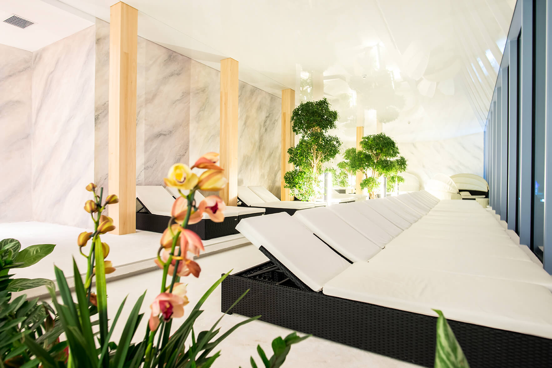 Liegestühle mit weißen Auflagen stehen geordnet in einem eleganten Spa-Raum.
