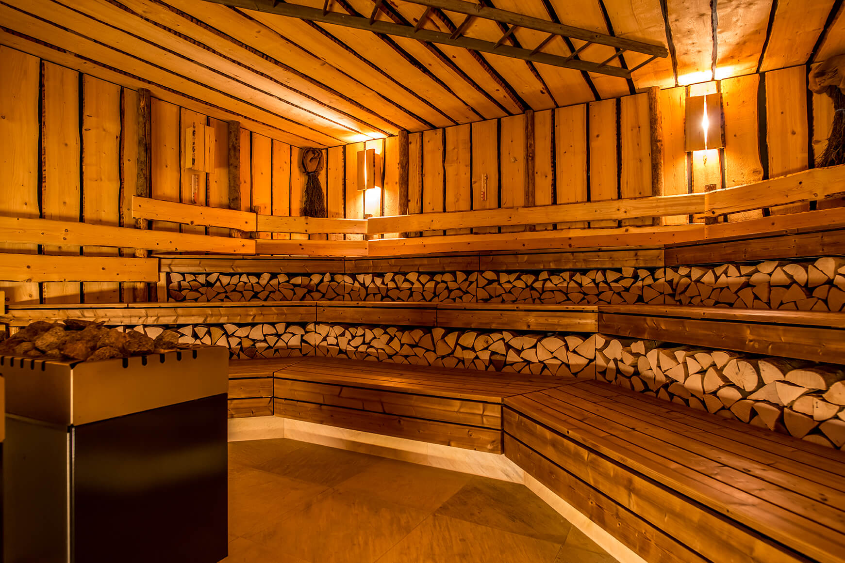 Saunaraum mit Holzbänken, warme Beleuchtung, gestapeltes Kaminholz.