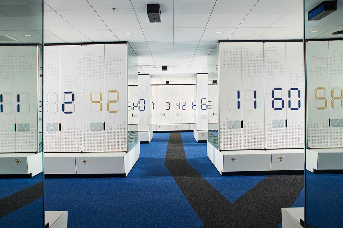 Weiße Schränke mit großen Zahlen in modernem Büroflur, blau-grauer Teppich.