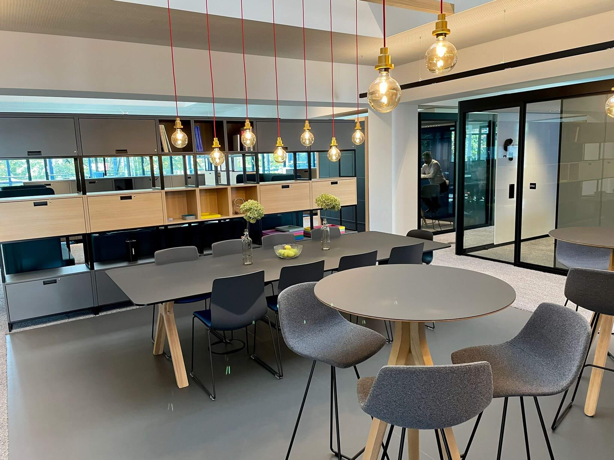 Moderner Pausenraum mit Tischen und Stühlen in einem offenen Raum mit Glastüren.