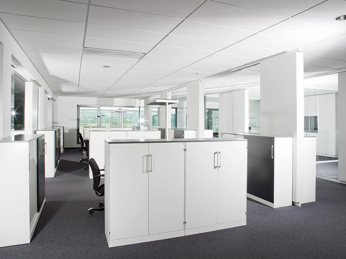 Weiße Schränke stehen in hellem Büro mit Fenstern.