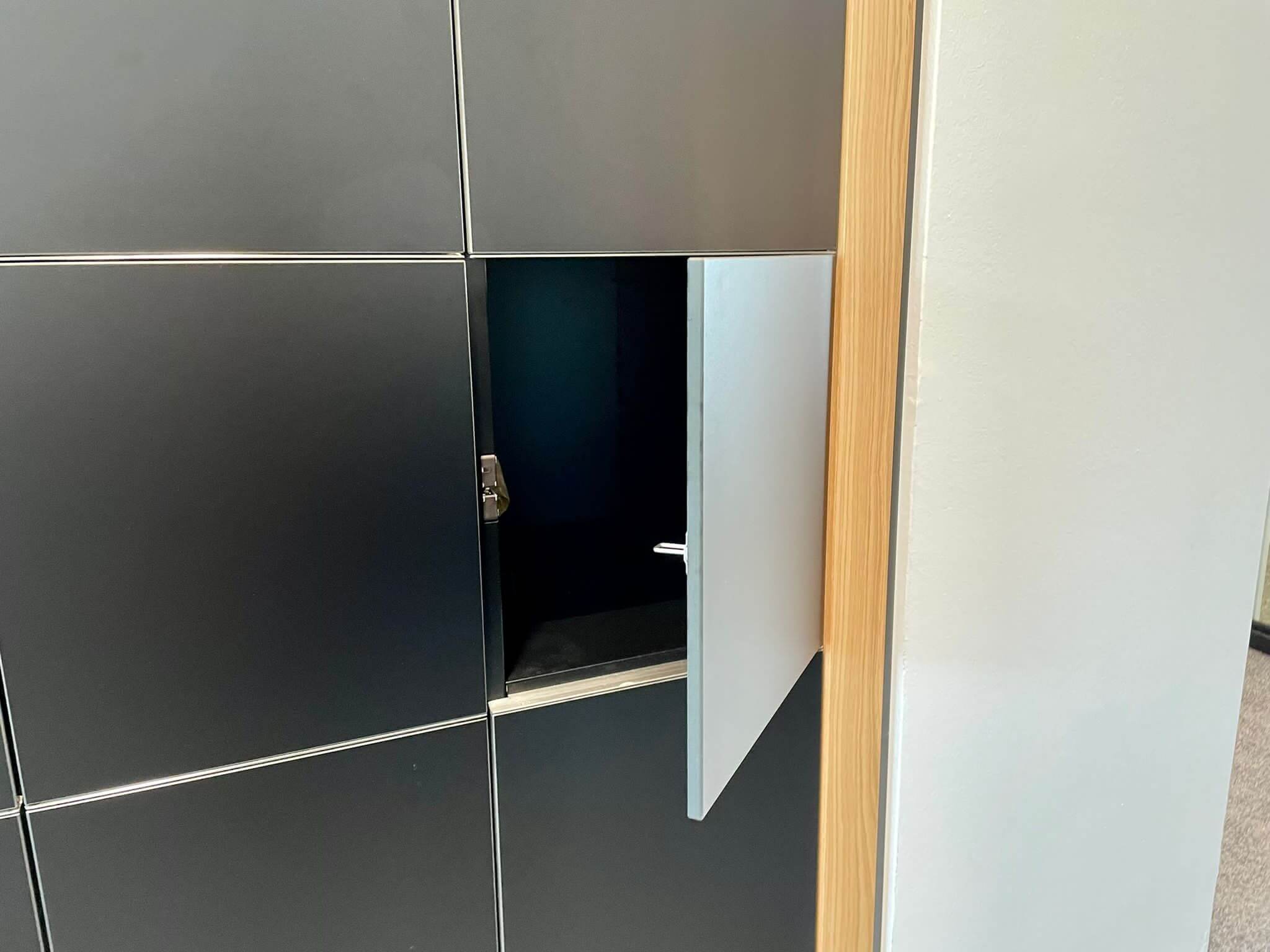 Geöffnetes schwarzes Schließfach mit sichtbarem Inhalt in Büroumgebung.